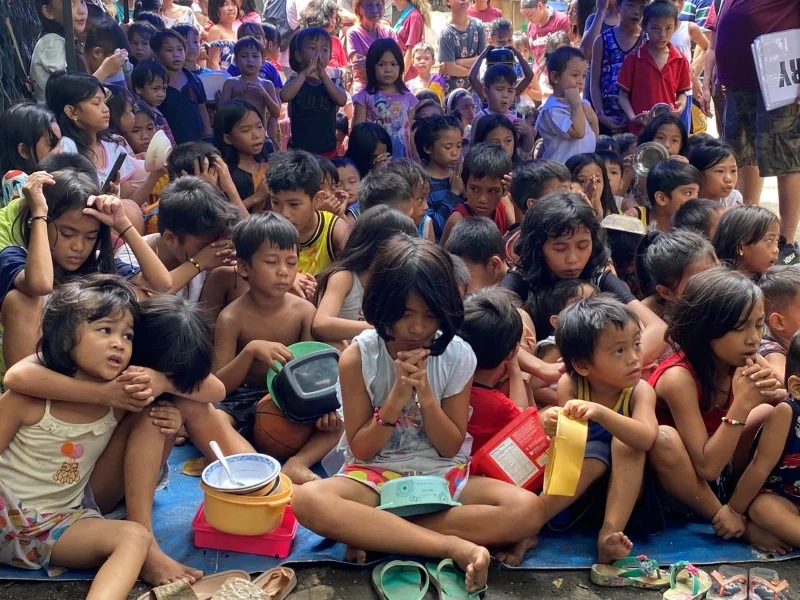 Children sitting close together on the floor, some holding bowls of food